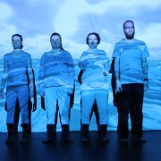 4 people on stage posing in front of an ocean background