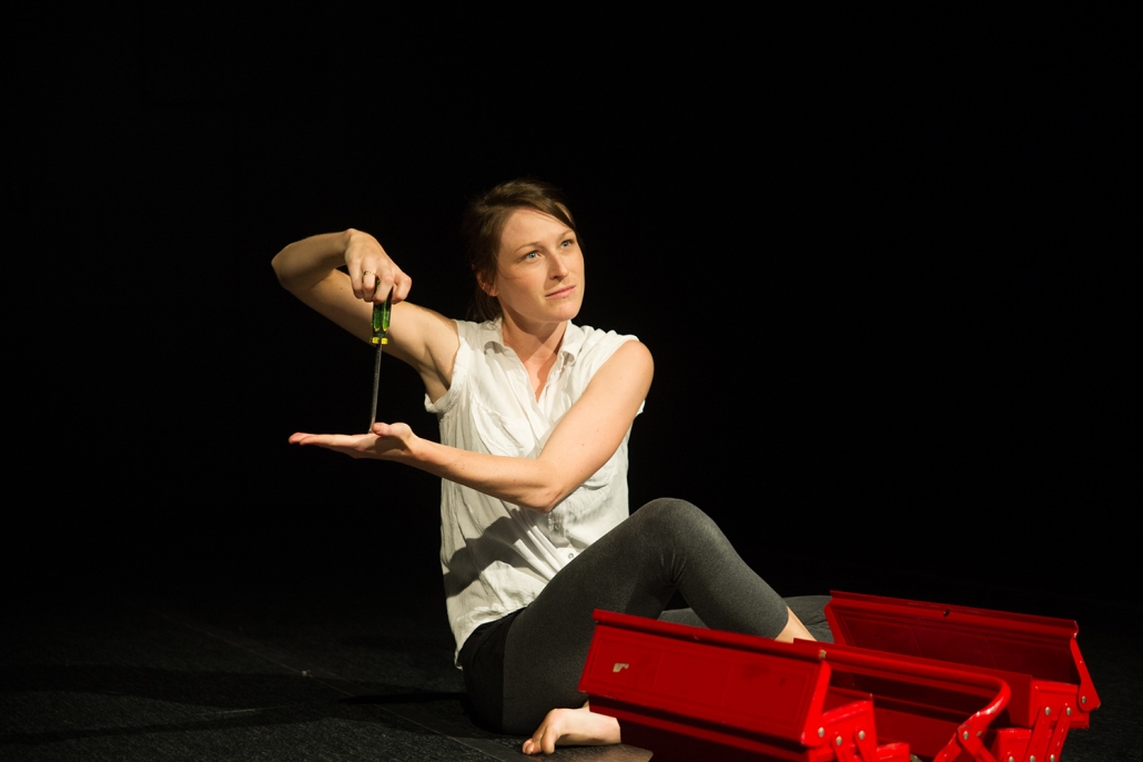 A woman poses on stage holding a screwdriver on to the palm of her hand