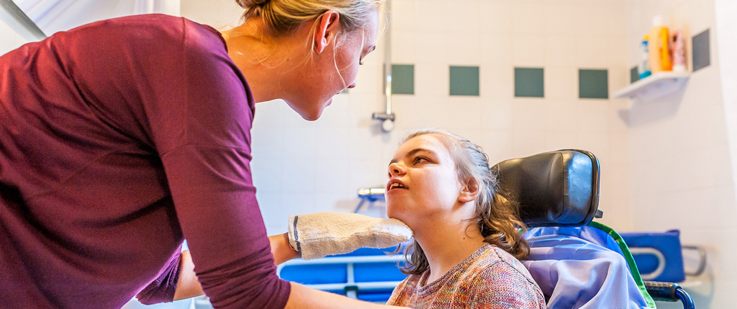 A woman in nurse scrubs assists a child with a disability