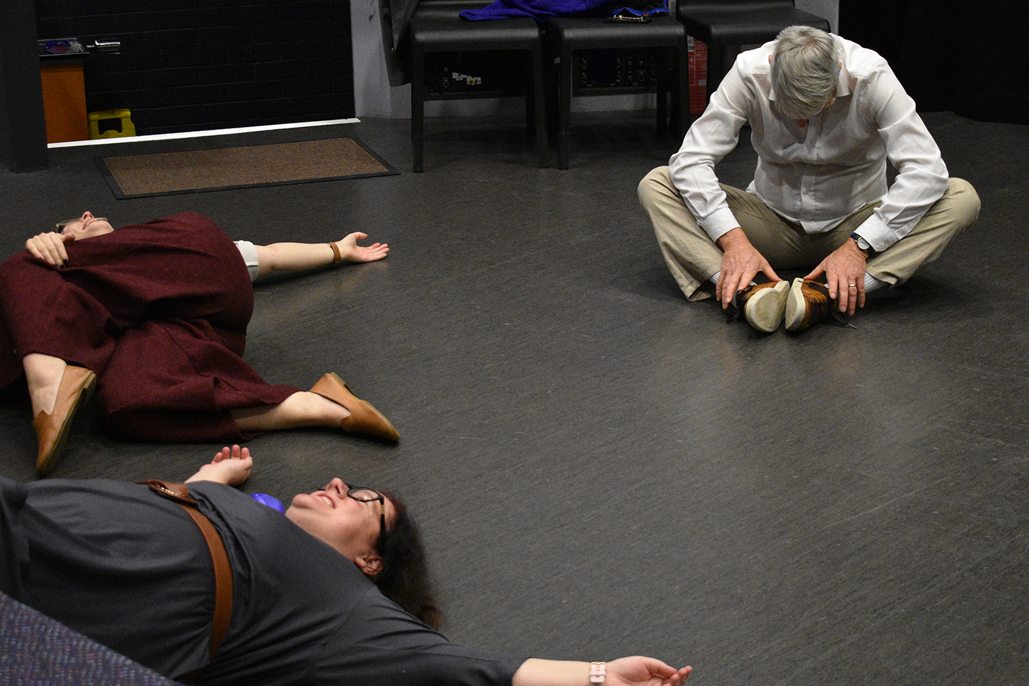 one man and two women do stretches in a rehearsal room