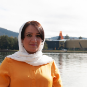 A woman in a head scarf looks at the Camera in front of a lake