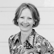 Black and white photo of a woman with short greying hair wearing a paisley shirt smiling at the camera