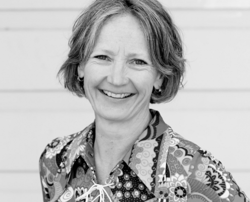 Black and white photo of a woman with short greying hair wearing a paisley shirt smiling at the camera