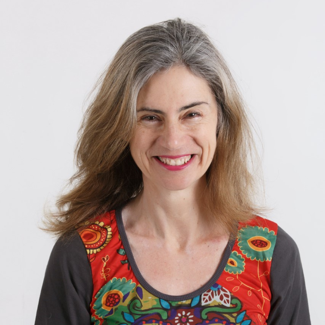 A woman with long brown hair wearing a paisley shirt smiles at the camera