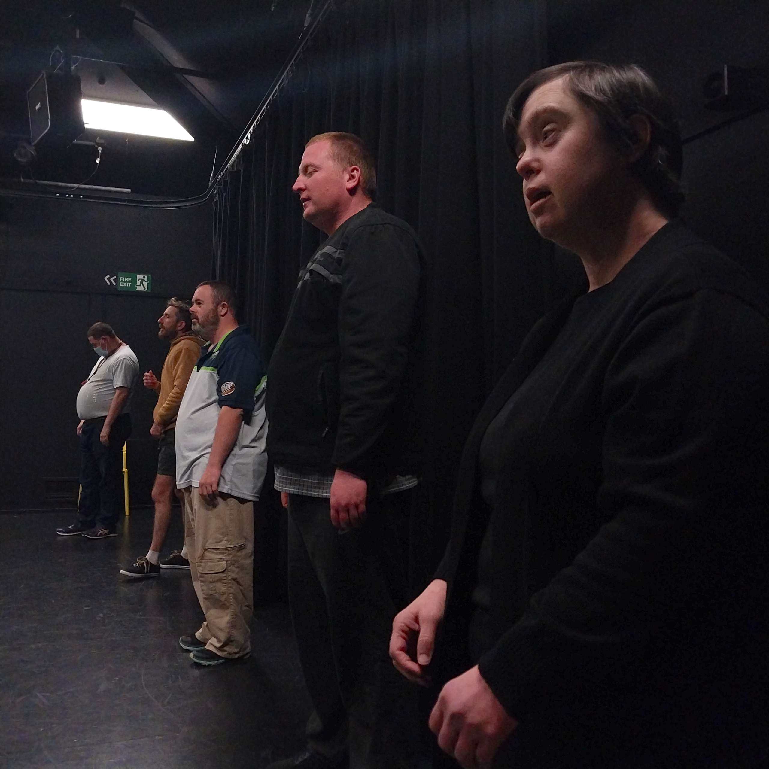 A group of men and women stand in a row facing forward about to start a drama exercise