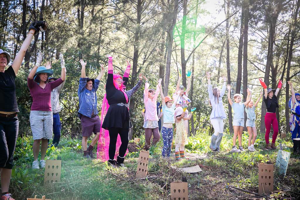 A group of people in various cosplay outfirs stand with their arms raised in the forest.