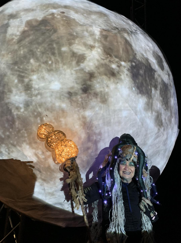 A woman in a sea creature costume poses in from of a lantern moon sculpture