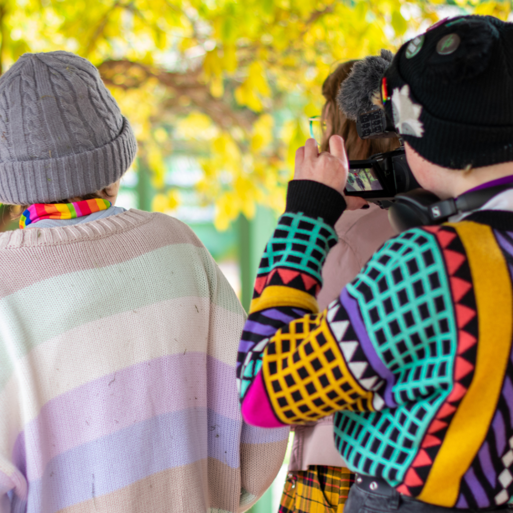 A group of young people in colourful clothes filming a scene outdoors