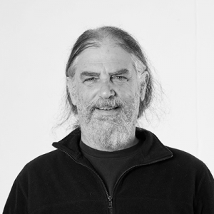 A man in a black shirt and jacket smiles at the camera