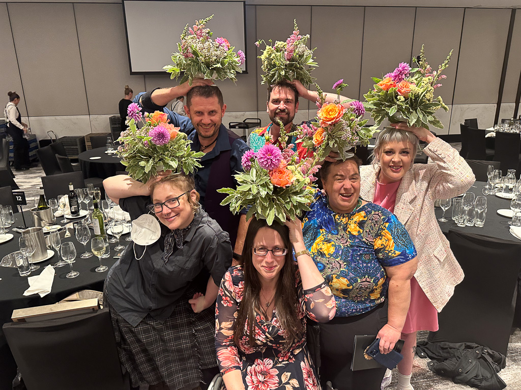 A group of people smile for the camera, each holding a flower arrangement above their heads.