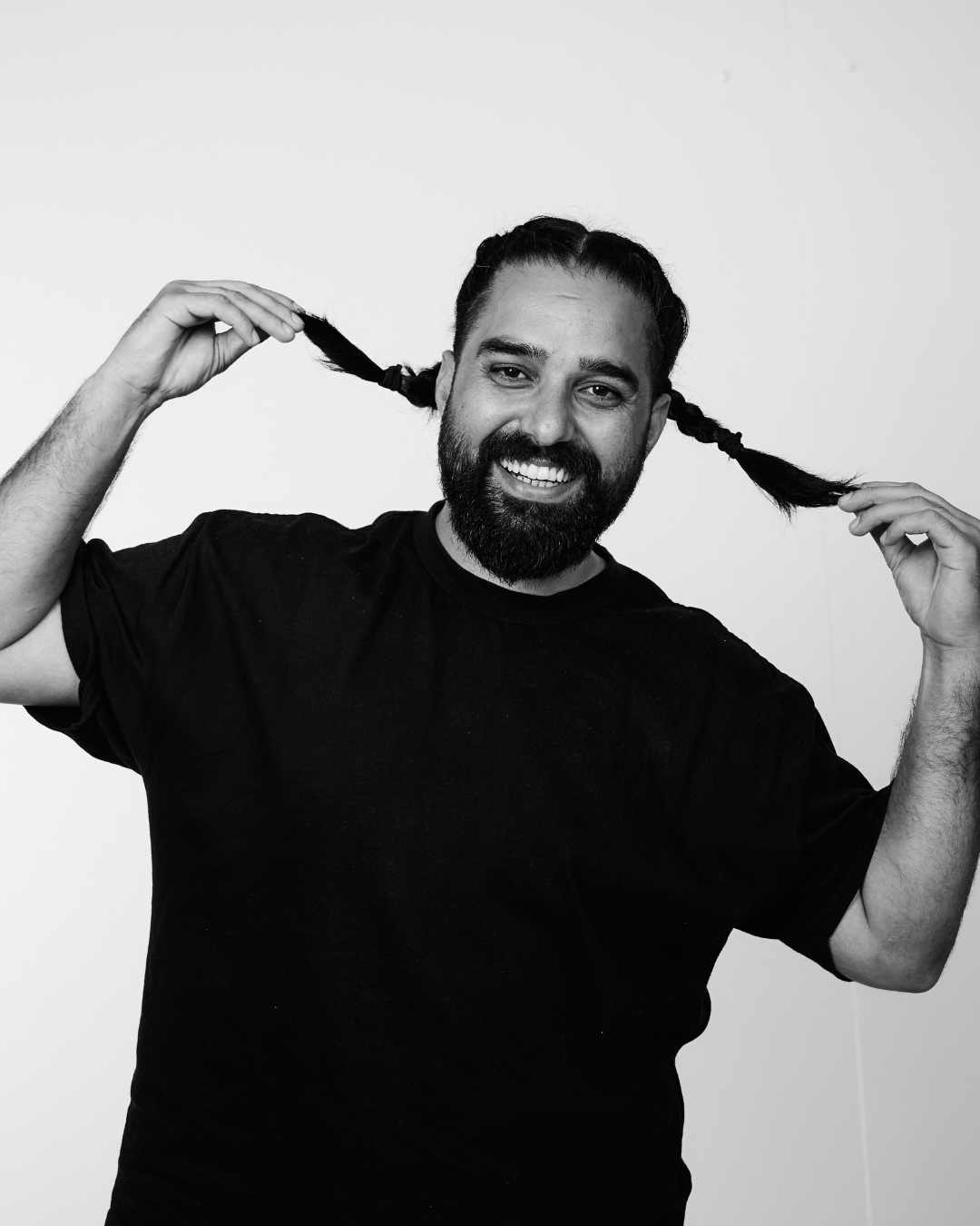 A man in a black shirt smiling at the camera pulling pigtail braids out to the side