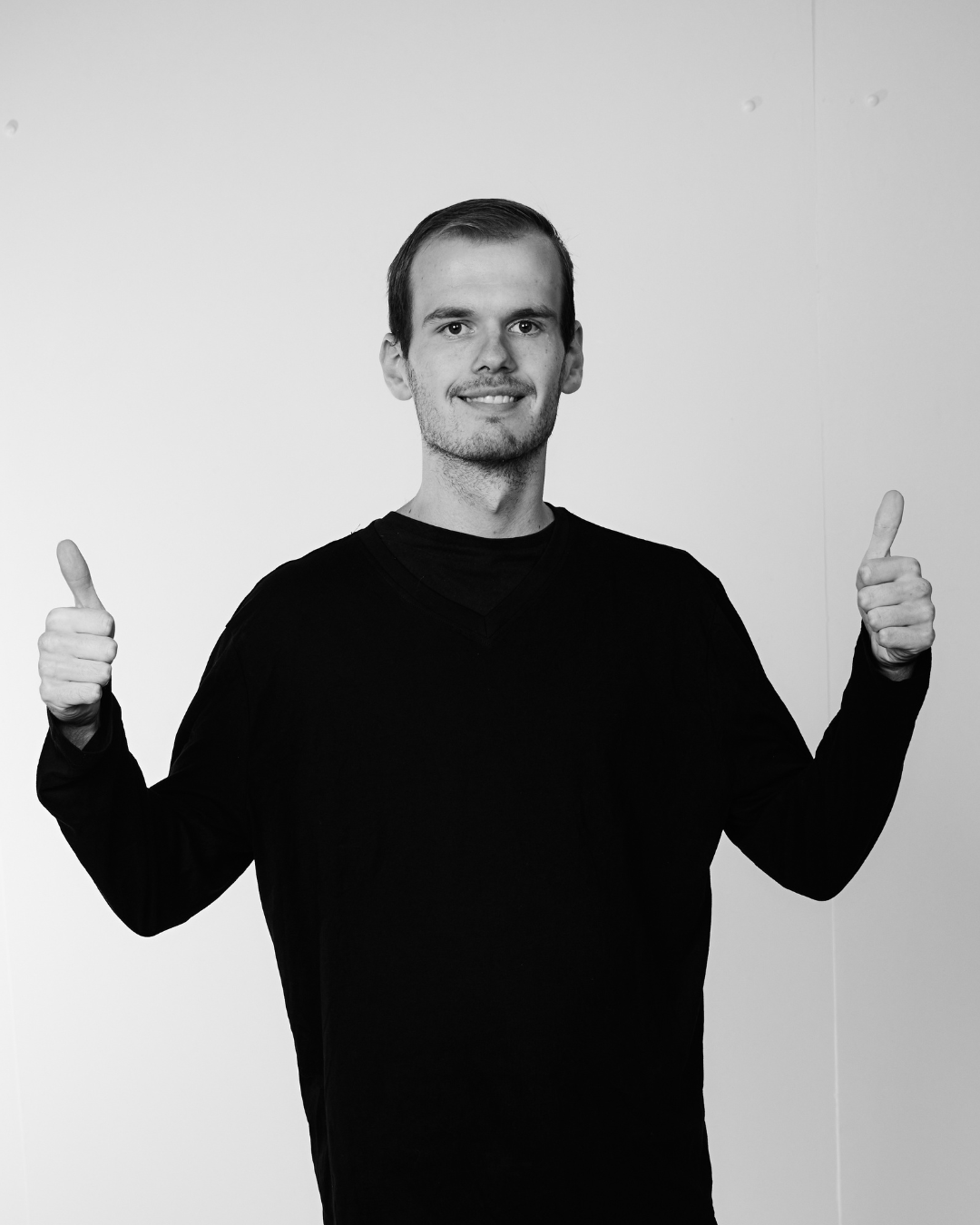 A man in a black shirt smiling at the camera hoolding both hands up with thumbs up