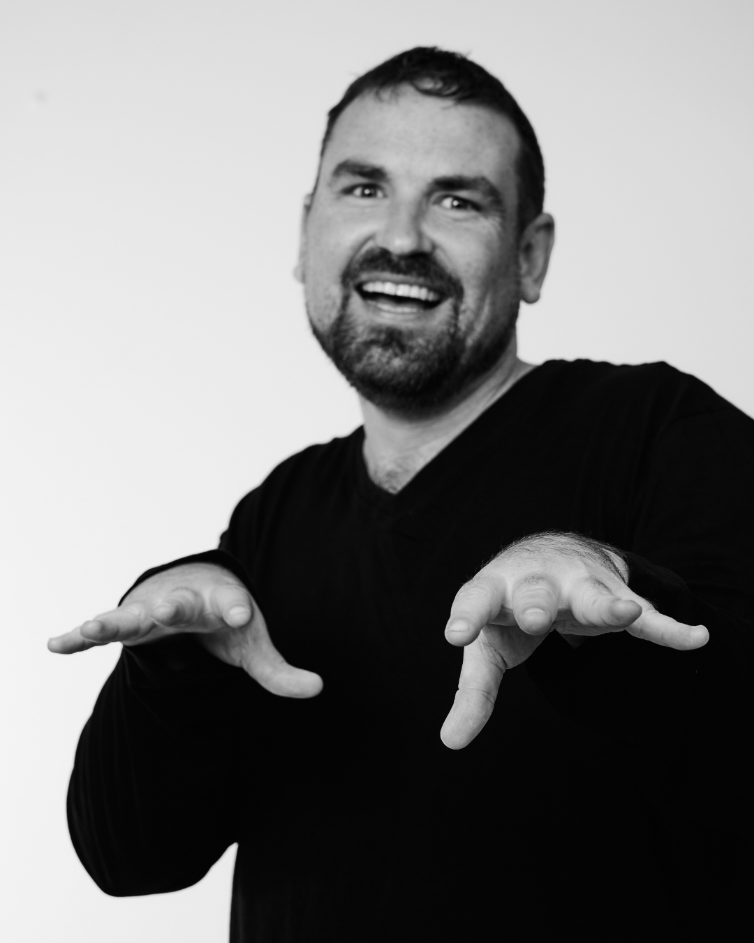 A man in a black shirt smiling at the camera hold hands palm down toward the camera with fingers spread