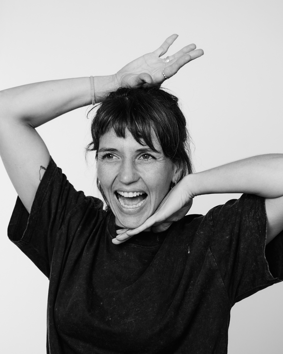 A woman in a black shirt smiling at the camera framing her face qith vogue hands