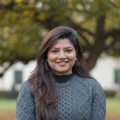 A woman in a blue sweater smiles at the camera on front of a large tree