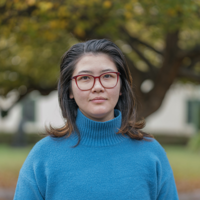 A persin in a blue sweater smiles at the camera on front of a large tree