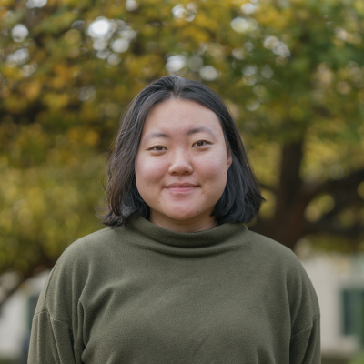 A woman in a green sweater smiles at the camera on front of a large tree