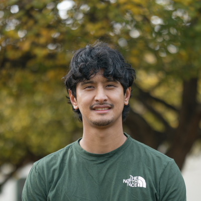 A Man in a green shirt smiles at the camera on front of a large tree